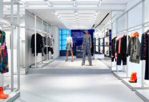 Foto di un negozio di abbigliamento. Ai lati ci sono abiti appesi e scarpe appoggiate sotto. Al centro due manichini. 