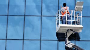 Tecnico professionista che pulisce vetrate alte con l'uso del cestello. 