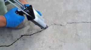 Mano con guanto che sigilla una crepa in un pavimento di cemento